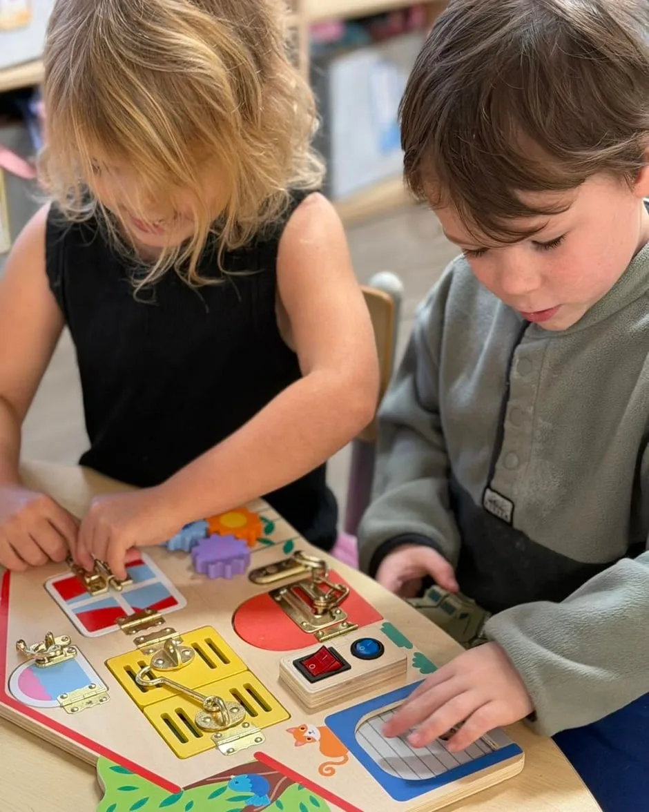 Two preschoolers working a wooden latch board together at Cherubs Nerang