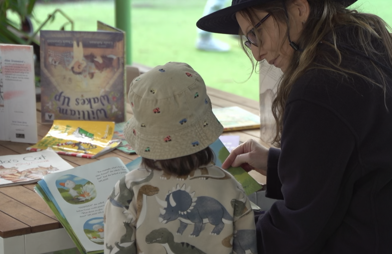 An Educator reading a picture book with a child at Cherubs Nerang