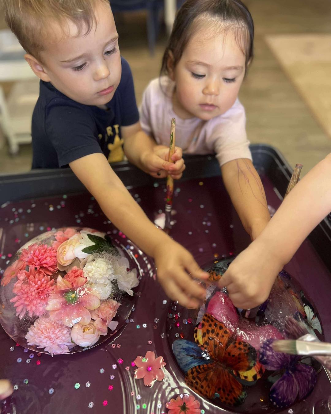 Two toddlers painting flowers frozen in ice at Cherubs Banora Point