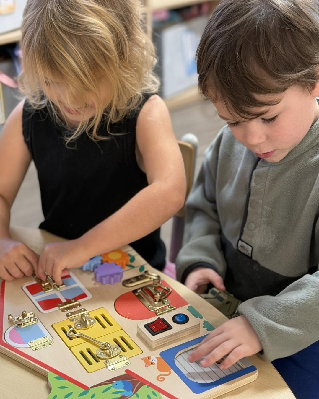 Two preschoolers working a wooden latch board together at Cherubs Nerang